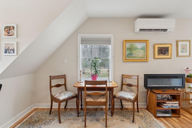 sitting room with baseboards, wood finished floors, lofted ceiling, and a wall mounted air conditioner