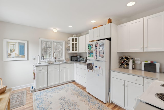 kitchen featuring black microwave, freestanding refrigerator, a sink, and white cabinetry