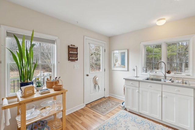 interior space featuring a sink, baseboards, light wood-style floors, and a healthy amount of sunlight