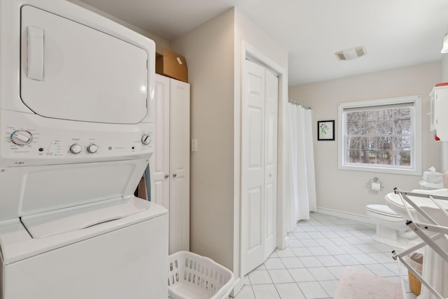 laundry room with laundry area, visible vents, stacked washing maching and dryer, baseboards, and light tile patterned floors