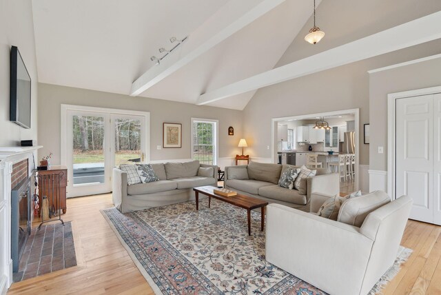 living room with a brick fireplace, high vaulted ceiling, and light wood finished floors