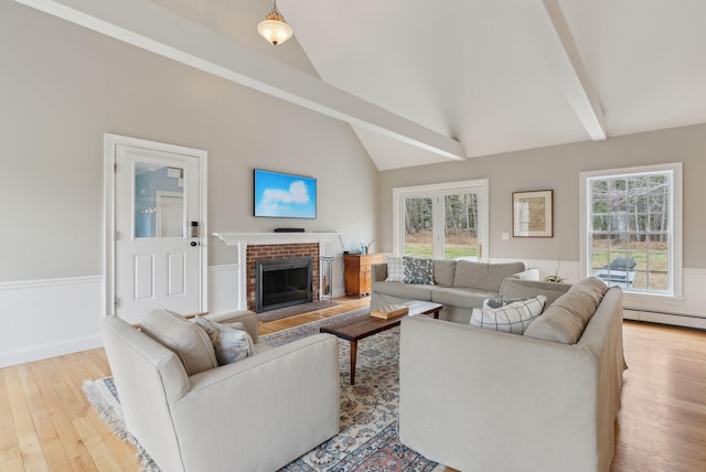 living area with a fireplace, lofted ceiling with beams, a wainscoted wall, and light wood-type flooring