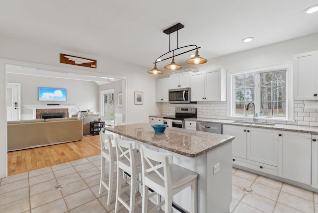 kitchen featuring decorative backsplash, a kitchen island, appliances with stainless steel finishes, a sink, and light tile patterned floors