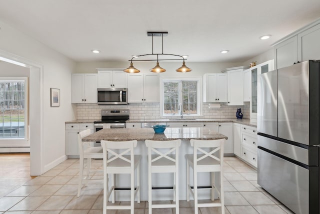 kitchen featuring appliances with stainless steel finishes, a sink, a kitchen breakfast bar, a center island, and backsplash