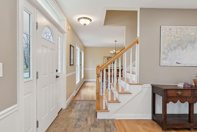 foyer entrance with an inviting chandelier, baseboard heating, wood-type flooring, stairs, and a wealth of natural light