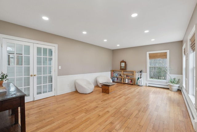 living area featuring a baseboard heating unit, french doors, light wood-style flooring, and a wainscoted wall