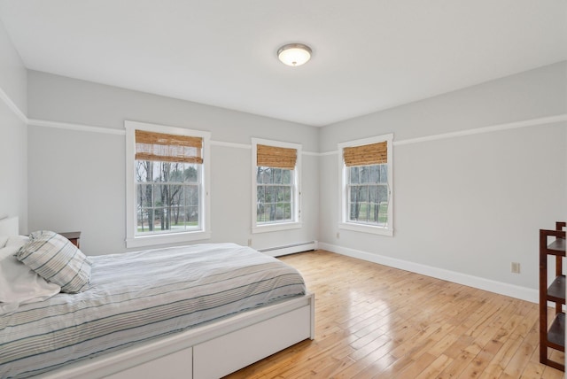 bedroom with light wood-style floors, baseboards, and a baseboard heating unit