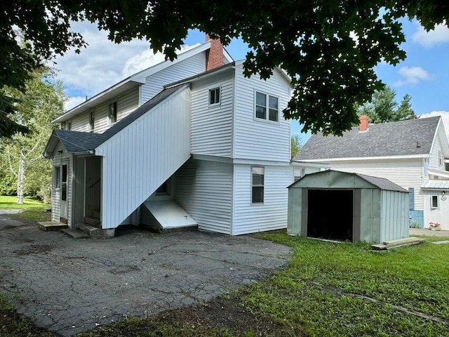 rear view of property with a chimney, an outdoor structure, and a shed