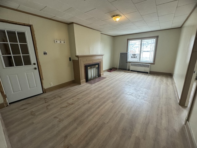 334 Main St, Madawaska, ME 04756 - unfurnished living room featuring radiator heating unit, light wood-style flooring, a fireplace with flush hearth, and baseboards