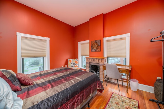 bedroom with a fireplace, wood finished floors, high vaulted ceiling, and baseboards