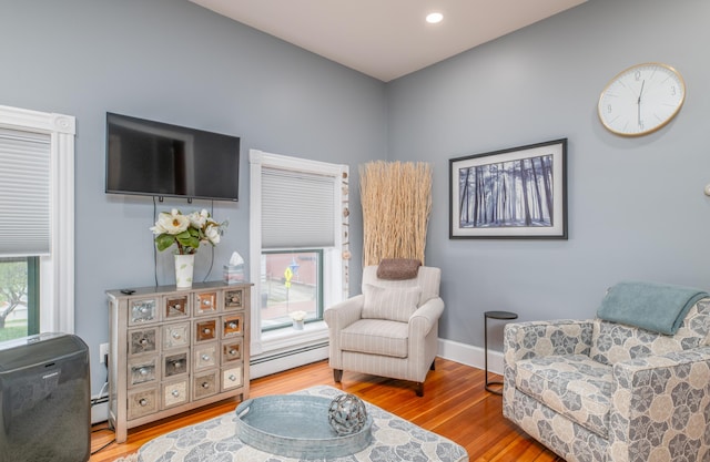 living area featuring wood finished floors, a baseboard heating unit, and baseboards
