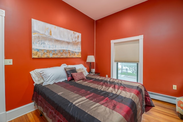 bedroom with a baseboard radiator, wood finished floors, and baseboards