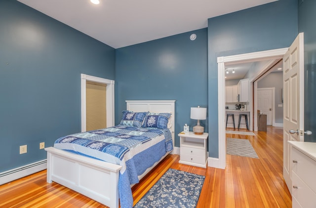 bedroom featuring baseboards, a baseboard heating unit, and light wood finished floors