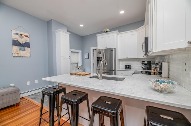 kitchen featuring a sink, a peninsula, white cabinetry, baseboard heating, and appliances with stainless steel finishes