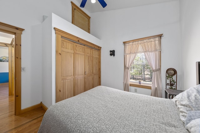 bedroom with a closet, baseboards, a towering ceiling, wood finished floors, and a ceiling fan