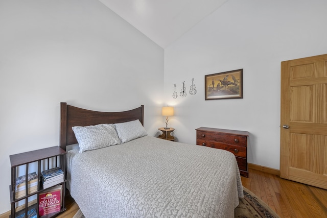 bedroom featuring wood finished floors, high vaulted ceiling, and baseboards
