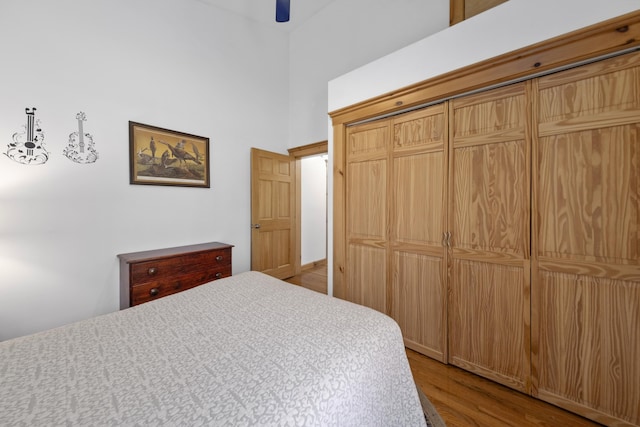 bedroom with wood finished floors, a ceiling fan, a high ceiling, and a closet