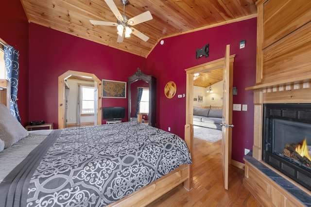 bedroom featuring lofted ceiling, arched walkways, wooden ceiling, a tile fireplace, and wood finished floors