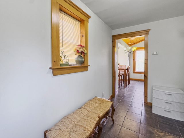corridor with dark tile patterned floors, baseboards, and an inviting chandelier