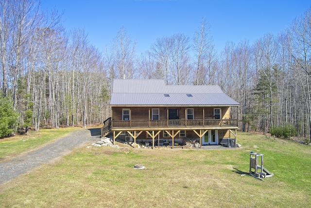rear view of house with metal roof, a wooden deck, a yard, and a forest view