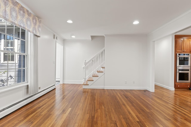 unfurnished living room with stairs, hardwood / wood-style floors, a baseboard heating unit, baseboards, and ornamental molding