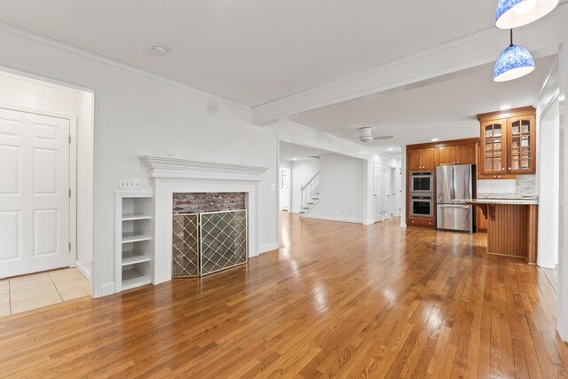 unfurnished living room with light wood-type flooring, baseboards, stairs, ceiling fan, and crown molding