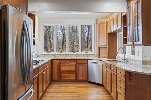 kitchen with light wood finished floors, stainless steel appliances, a sink, glass insert cabinets, and light stone counters