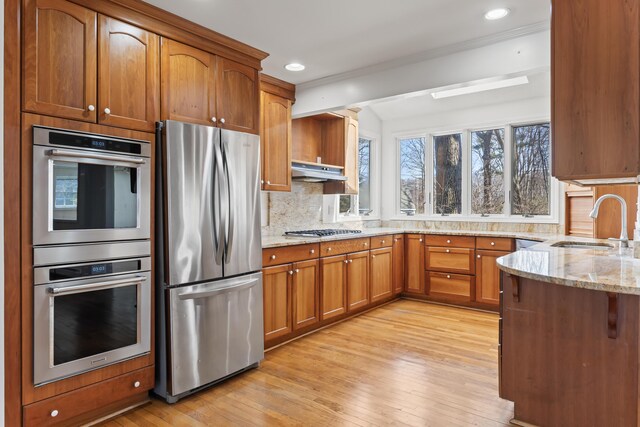 kitchen with a sink, light stone countertops, decorative backsplash, light wood-style flooring, and appliances with stainless steel finishes