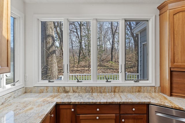 kitchen with dishwasher, brown cabinets, a wealth of natural light, and light stone countertops