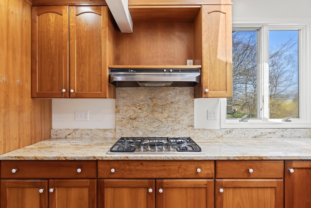 kitchen with stainless steel gas stovetop, under cabinet range hood, light stone countertops, and tasteful backsplash