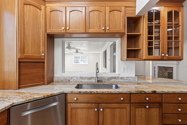 kitchen featuring glass insert cabinets, stainless steel dishwasher, a sink, and light stone counters