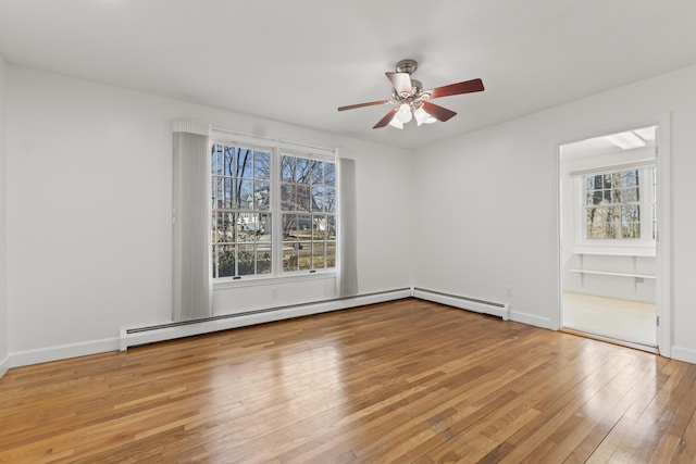 empty room with a baseboard radiator, a wealth of natural light, a ceiling fan, and hardwood / wood-style floors