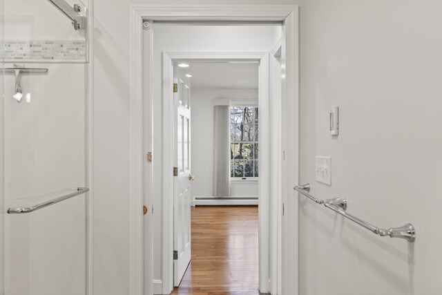 hallway with a baseboard heating unit and wood finished floors