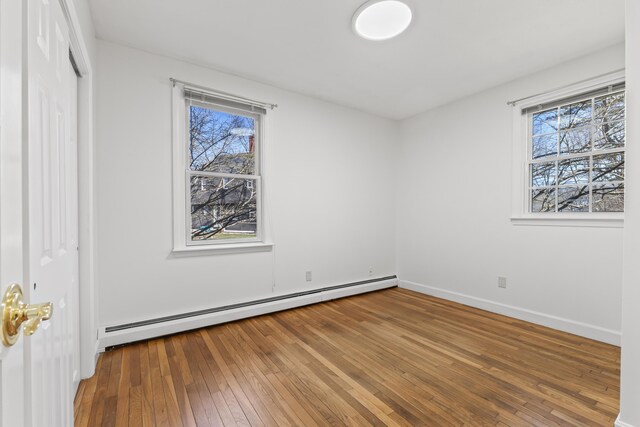 unfurnished bedroom featuring baseboard heating, wood-type flooring, baseboards, and multiple windows