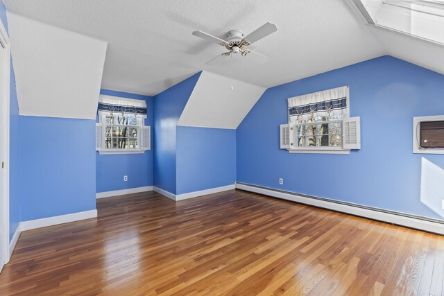 additional living space featuring lofted ceiling, wood finished floors, a ceiling fan, a wall unit AC, and baseboard heating