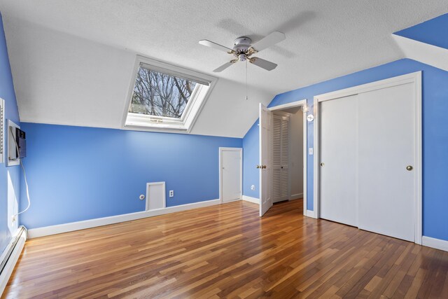 additional living space with a baseboard radiator, a ceiling fan, vaulted ceiling with skylight, wood finished floors, and a textured ceiling