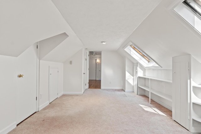additional living space featuring light carpet, lofted ceiling with skylight, and baseboards