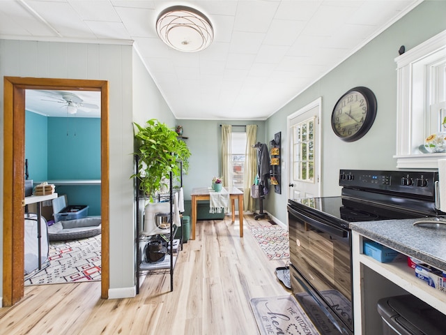 kitchen with light wood-type flooring, crown molding, black electric range oven, and baseboards