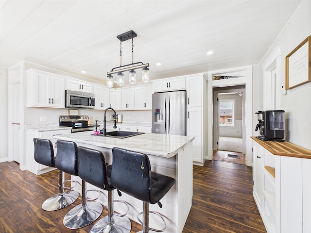 kitchen featuring white cabinets, a sink, appliances with stainless steel finishes, dark wood-style floors, and a center island with sink