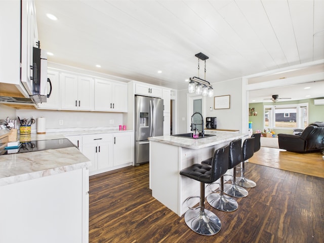 kitchen with a sink, stainless steel appliances, a kitchen bar, white cabinetry, and dark wood finished floors