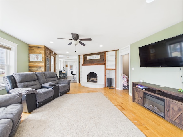 living area with ceiling fan, a fireplace with raised hearth, recessed lighting, and light wood-style floors
