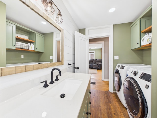 laundry room featuring recessed lighting, cabinet space, dark wood-style flooring, washing machine and dryer, and a sink