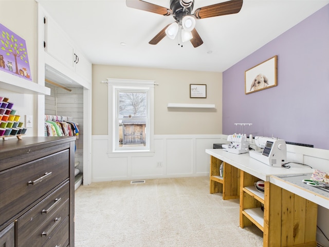 office featuring a wainscoted wall, a ceiling fan, light colored carpet, and visible vents