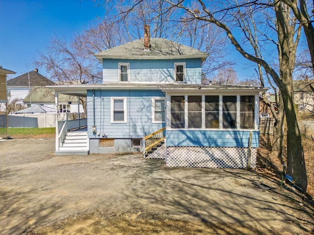 back of house featuring a chimney, a sunroom, fence, and roof with shingles