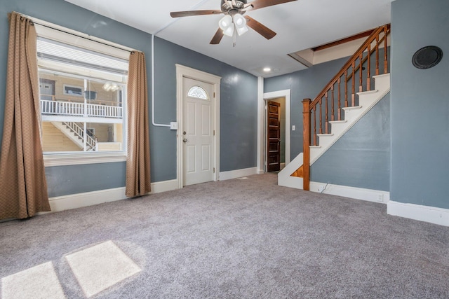 foyer entrance featuring stairway, carpet flooring, a ceiling fan, and baseboards