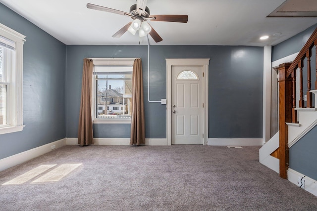 carpeted foyer featuring baseboards, stairs, and ceiling fan