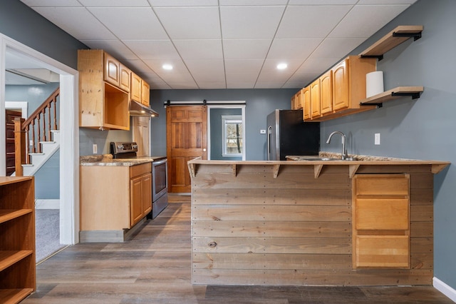 kitchen with a barn door, under cabinet range hood, stainless steel appliances, open shelves, and a peninsula