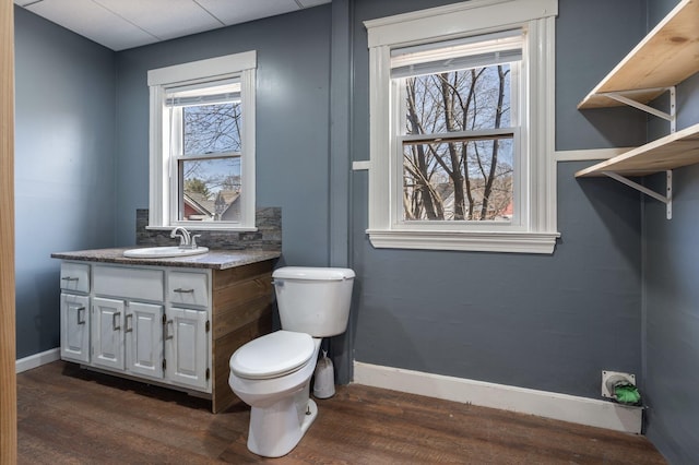bathroom with toilet, vanity, wood finished floors, and baseboards