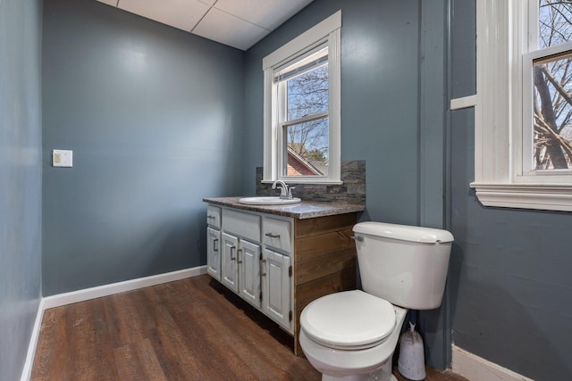 half bathroom with baseboards, wood finished floors, plenty of natural light, and toilet