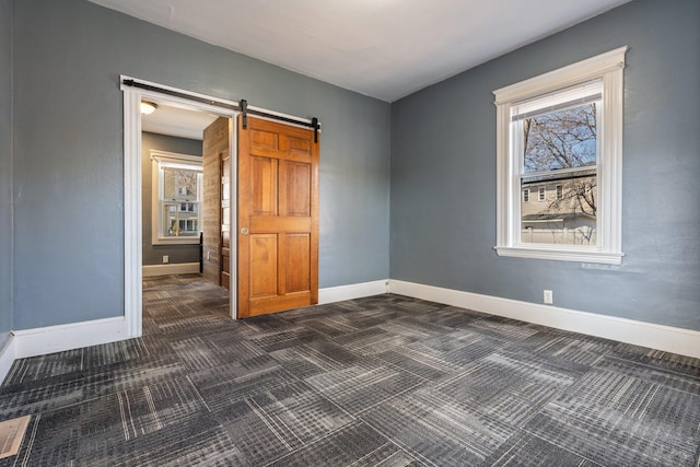 empty room with a barn door, baseboards, and dark colored carpet